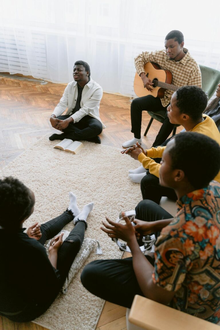 A diverse group of people gathered indoors for prayer and music, featuring a guitarist leading worship.