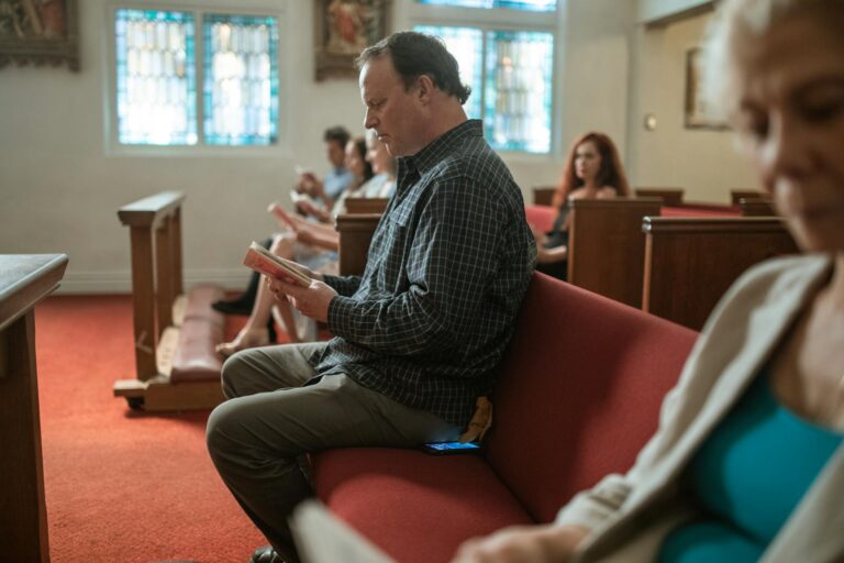 A group of diverse adults reading in a church's serene interior setting.